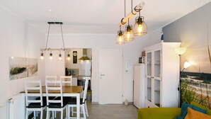 A modern living room with a dining area, a green sofa, and a kitchen in the background. - Holiday Apartment 'Ferienhaus Deichblick Nessmersiel' with Private Terrace, Garden & Wi-Fi (Dornum)