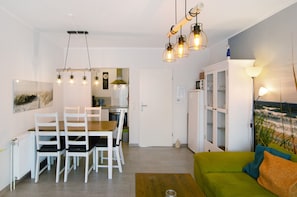 A modern living room with a dining area, a green sofa, and a kitchen in the background.