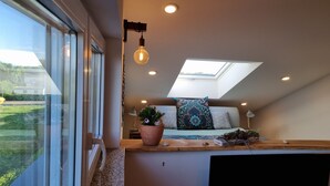 Een compacte slaapkamer met dakraam, een kamerplant en een houten plank.