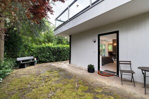 A modern building with a patio area, a bench, a chair, and a small potted plant.