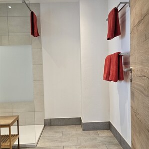 Ein Badezimmer mit Dusche, einem Handtuchhalter mit roten Handtüchern und einer Wand mit Holzvertäfelung.