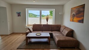 A living room with a brown sofa, a wooden coffee table, and a view of a green landscape through large windows.