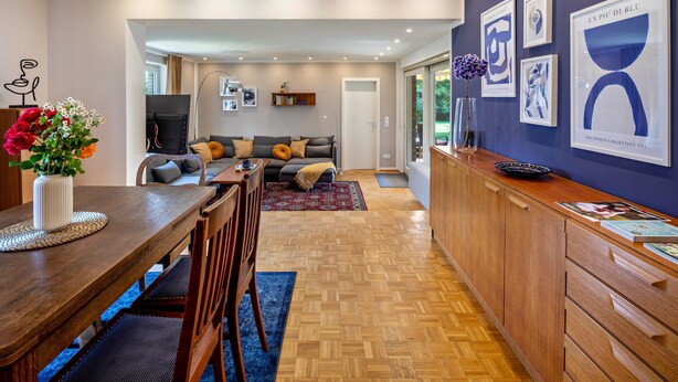 A modern kitchen with a dining area, wooden cabinets, and a large window.