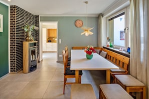 A dining area with a white table, wooden benches, a clock on the wall, and a window with curtains. - Spacious Holiday Home in Northern Hesse with Private Terrace, Garden & Wi-Fi (Homberg (Efze))