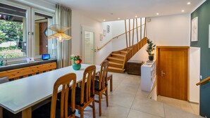 A modern kitchen with a wooden staircase, a dining area with wooden chairs, and a view of the outdoors.