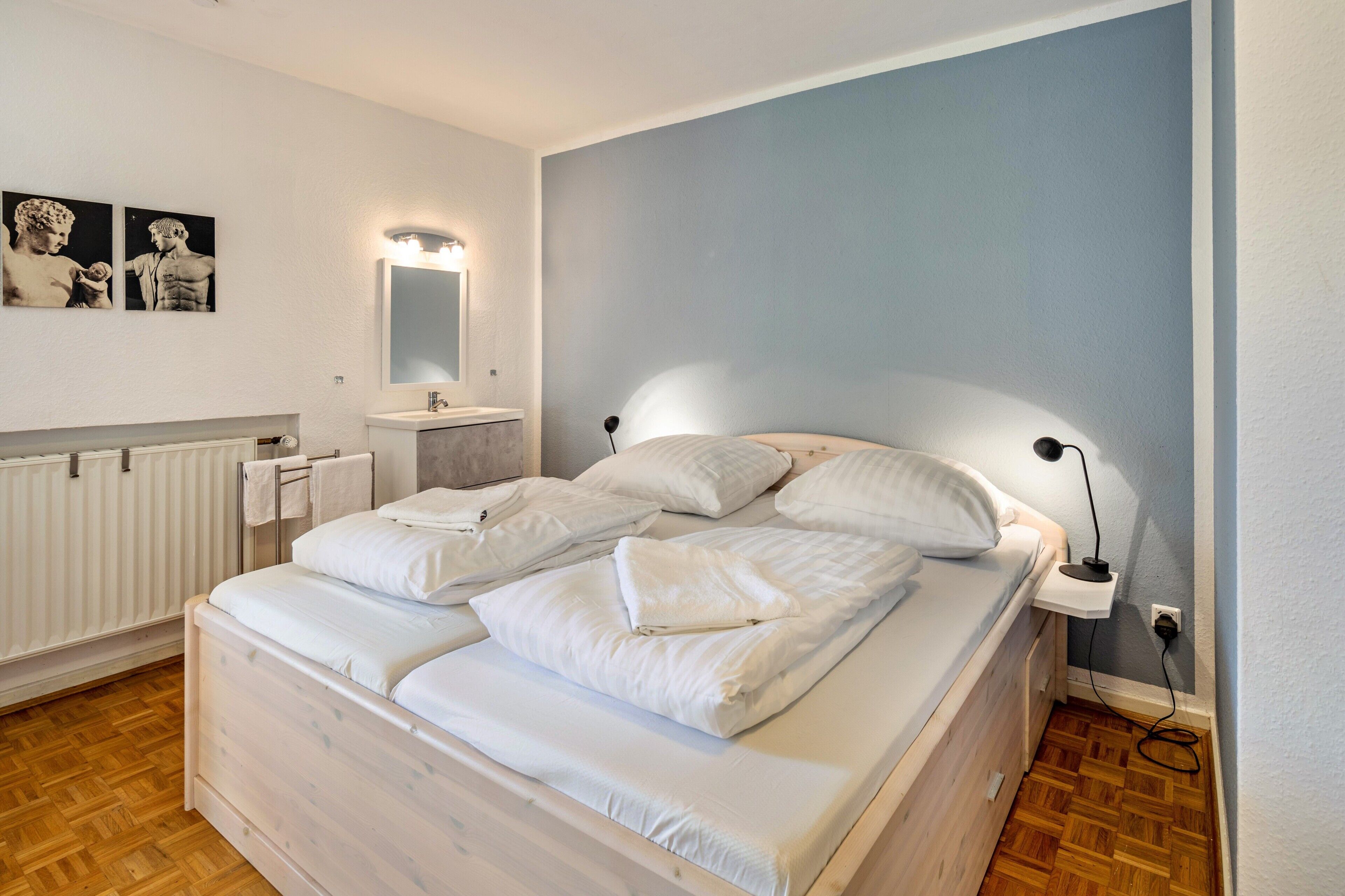 A bedroom with a bed, bedside table, lamp, and wall-mounted mirror.