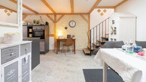 Una cocina compacta con pared de piedra, vigas de madera, zona de comedor con mesa y sillas, y una escalera.