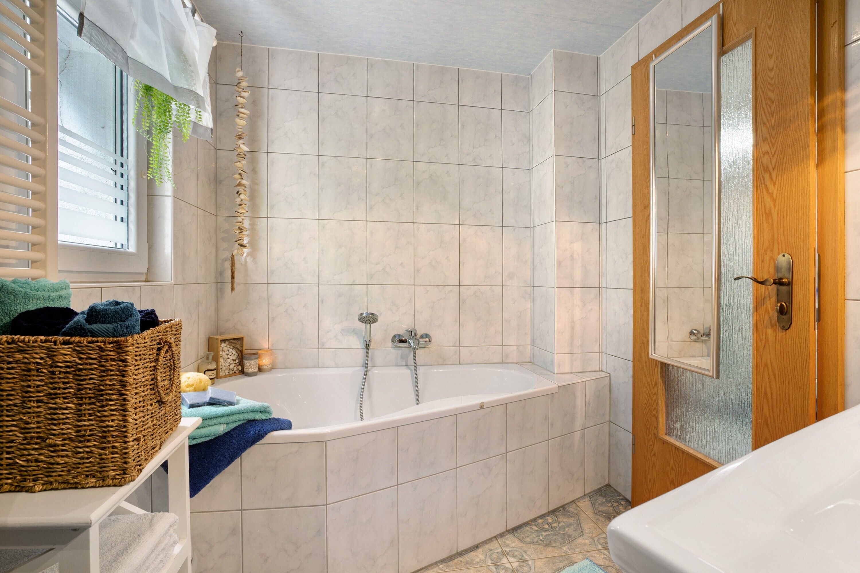 A bathroom with a bathtub, a wooden door, and a wicker basket on a white shelf.