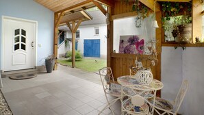 Un patio techado con una mesa y sillas, una puerta blanca y una cerca azul al fondo.