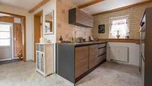 Una cocina con una isla central, armarios de madera, un muro decorativo de piedra, una ventana con una planta y un radiador.