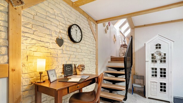 Una habitación con pared de piedra, escritorio de madera, silla y una puerta blanca adornada con un adorno.