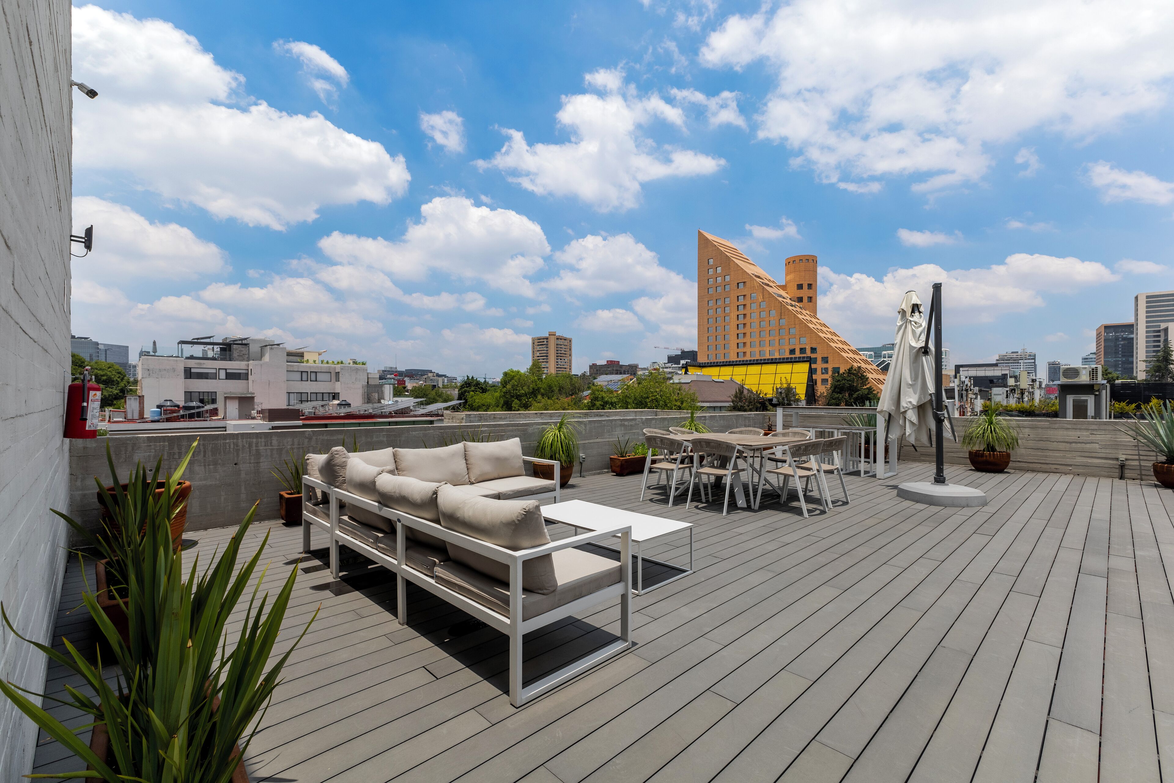 Une terrasse sur le toit, aménagée avec un canapé, une table et des chaises, et entourée de plantes en pot.