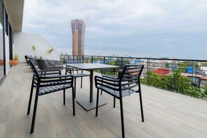 Een balkon met een tafel en stoelen, een potplant en uitzicht op een hoog gebouw en stadsbeeld.