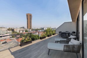 Une terrasse sur le toit offrant une vue sur un immeuble de grande hauteur, avec des sièges en plein air et des plantes en pot.