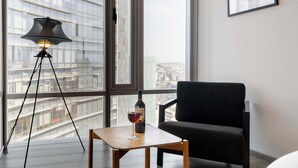 A modern room with a large window, a floor lamp, a chair, and a table with a wine glass and bottle.