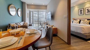 A modern hotel room with a dining area, a sofa, a bed, and a TV.