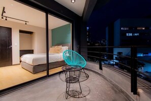 Un dormitorio moderno con una cama, una silla azul y un balcón con vistas a la ciudad.