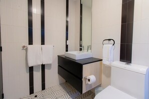Une salle de bain moderne avec un mur recouvert de carreaux noirs et blancs, un lavabo blanc avec un miroir au-dessus, et des toilettes avec un porte-serviettes.
