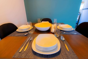 Enjoy meals with family and friends at this dining table for four, complete with a central bowl, plates, glasses, and cutlery.