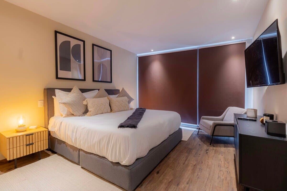 Ein modernes Schlafzimmer mit einem großen Bett, Nachttischen, einem Schreibtisch und einem Fernseher.