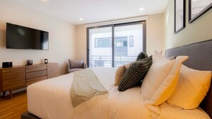 Un dormitorio moderno con una cama grande, un televisor de pantalla plana, un aparador de madera y vistas al balcón.