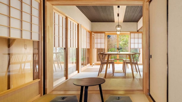 Una habitación japonesa tradicional con suelo de tatami, una mesa baja y vistas de un jardín a través de puertas correderas.