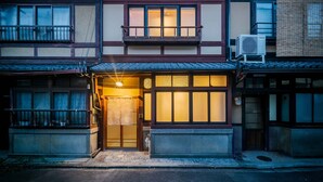 Una casa tradicional japonesa con entrada de madera, un balcón y una unidad de aire acondicionado visible.