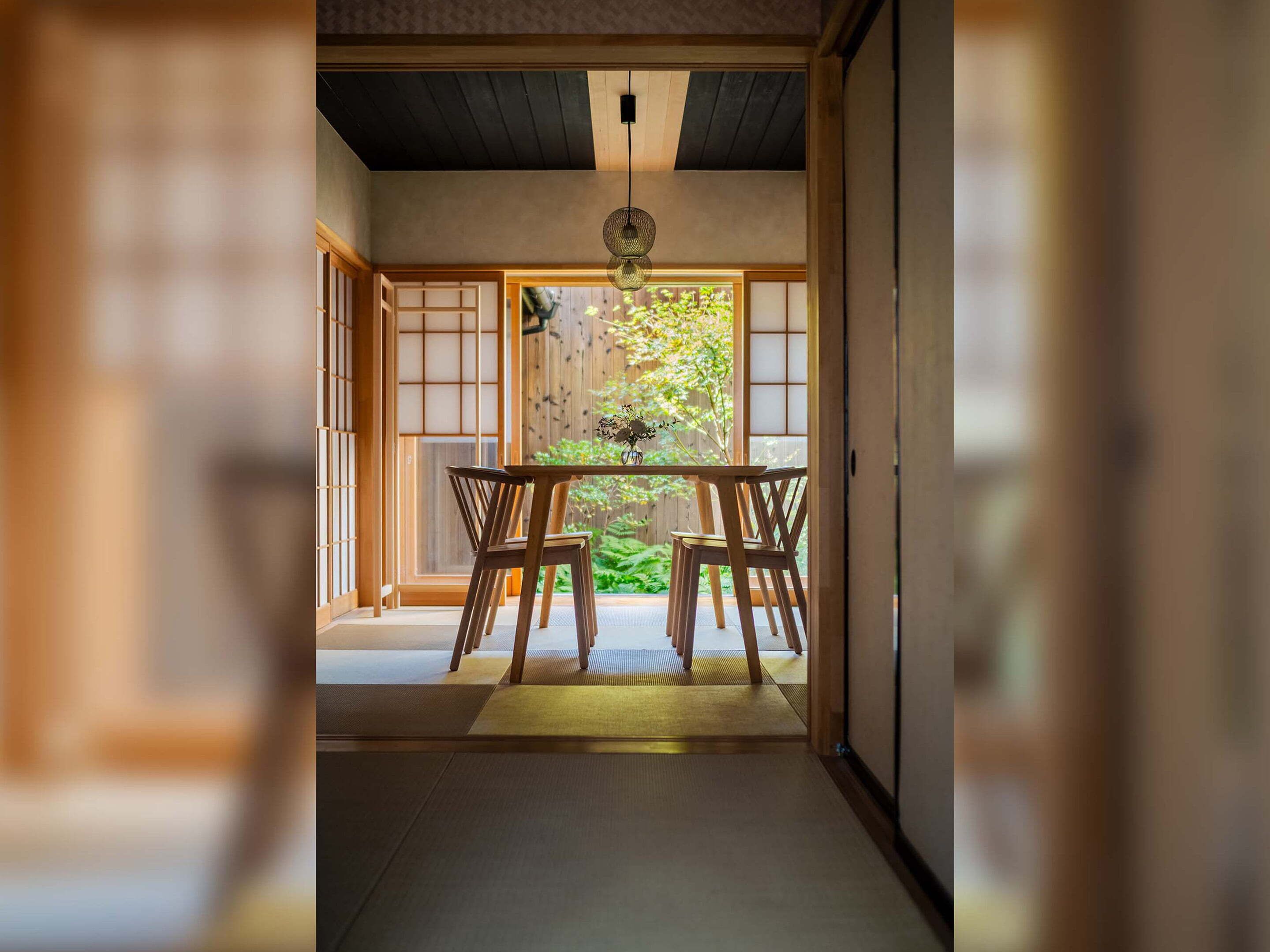 Een traditionele Japanse kamer met tatami vloeren, een lage tafel met stoelen, en een schuifdeur naar een tuin.