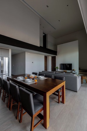 A modern dining area with a wooden table, chairs, and a television in the background.
