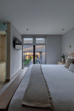 A modern bedroom with a large bed, a TV mounted on the wall, and a view of the outside.