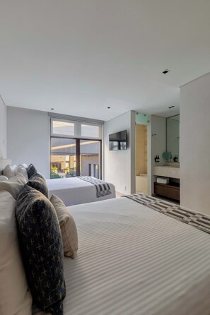 A modern bedroom with a large bed, a TV mounted on the wall, and a bathroom visible through an open door.