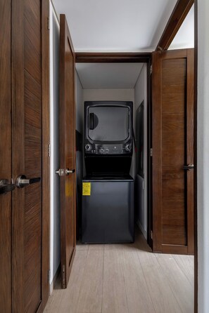A compact, dark-colored laundry room with a built-in washer and dryer, wooden doors, and a tiled floor.