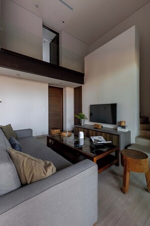 Ein modernes Wohnzimmer mit einem grauen Sofa, einem Couchtisch, einem Fernseher und einer Treppe, die in einen oberen Bereich führt.