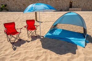 Ein Strand mit zwei roten Klappstühlen und einem blauen Zelt.