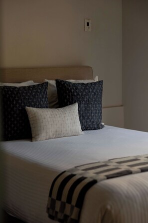 Una cama con un colchón blanco y una colcha a rayas, acompañada de tres almohadas con distintos diseños.