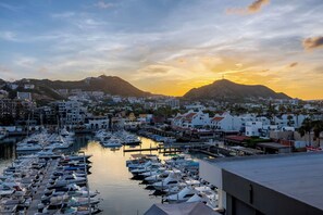A marina with numerous boats docked, surrounded by buildings and a mountain in the background.
