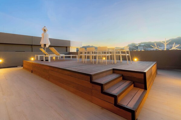 A rooftop terrace with a wooden deck, outdoor seating, and a view of the cityscape.
