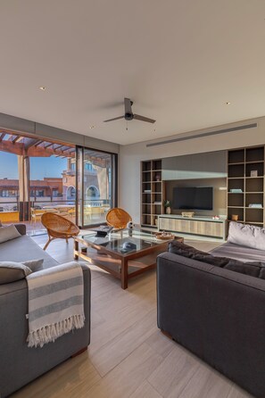 Una sala moderna con una mesa de centro de vidrio, dos sofás, un televisor y una estantería.