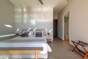 Une chambre à coucher moderne avec un grand lit, des tables de chevet, un banc et une vue sur le couloir.