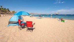Une plage avec une tente, des chaises rouges et une vue dégagée sur l’océan et les bateaux.