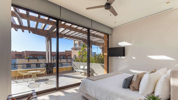 Une chambre moderne dotée d’un grand lit, d’une télévision et d’un balcon aménagé avec du mobilier d’extérieur.