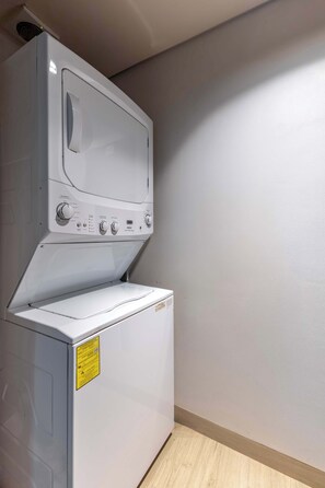 Eine gestapelte Waschmaschine und ein Trockner in einer Ecke, mit Holzboden und schlichter Wand.