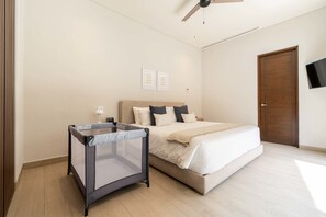 Ein Schlafzimmer mit einem Bett, einem Deckenventilator, einem an der Wand montierten Fernseher und einer Tür.