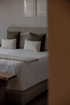 A neatly made bed with a white comforter and multiple pillows, a wooden headboard, and a bedside table.