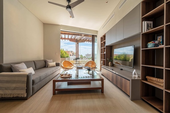 A modern living room with a sofa, coffee table, wicker chairs, a TV, and a bookshelf.