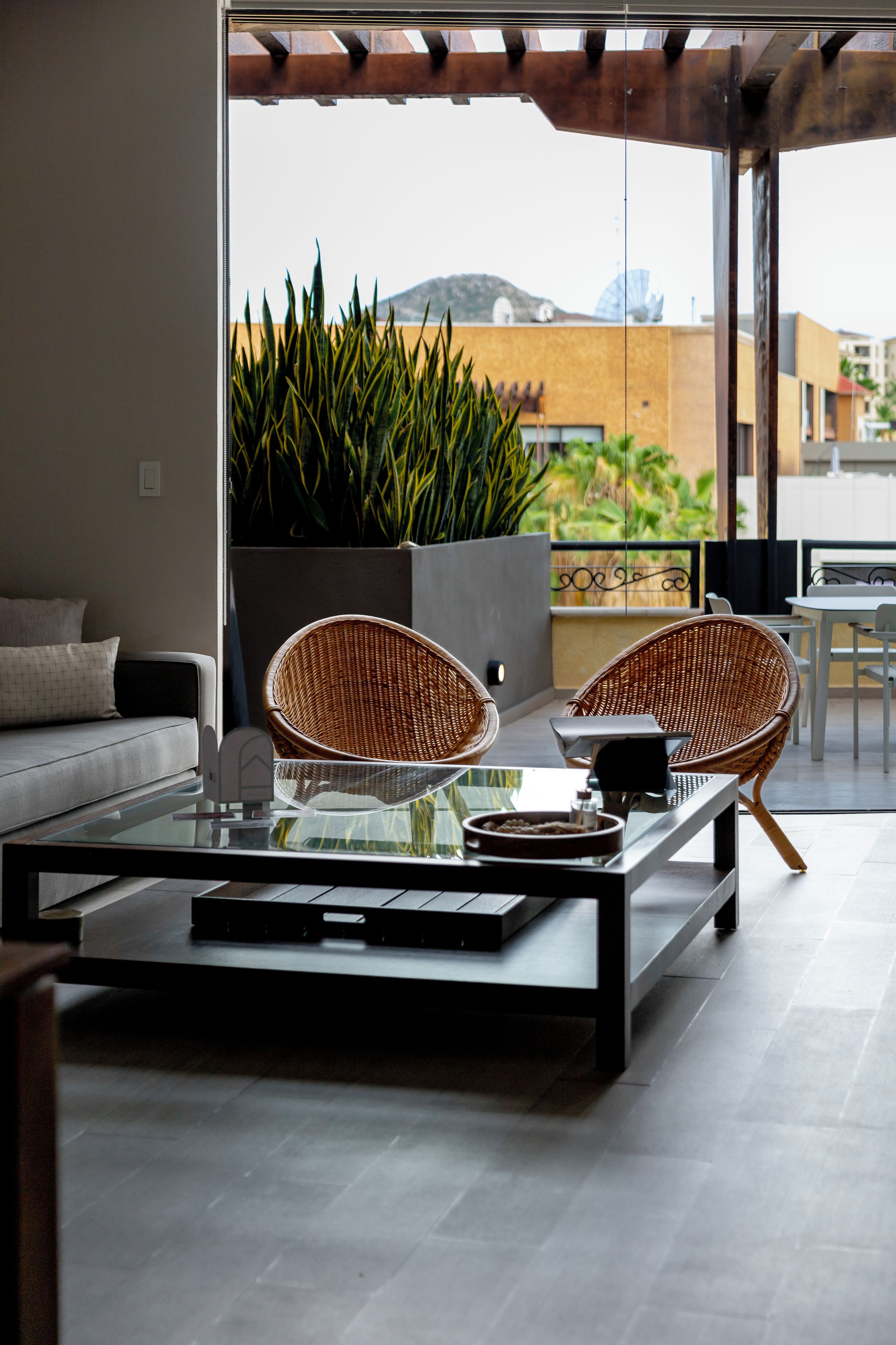 A modern outdoor seating area with a glass-top table, two wicker chairs, and a potted plant.
