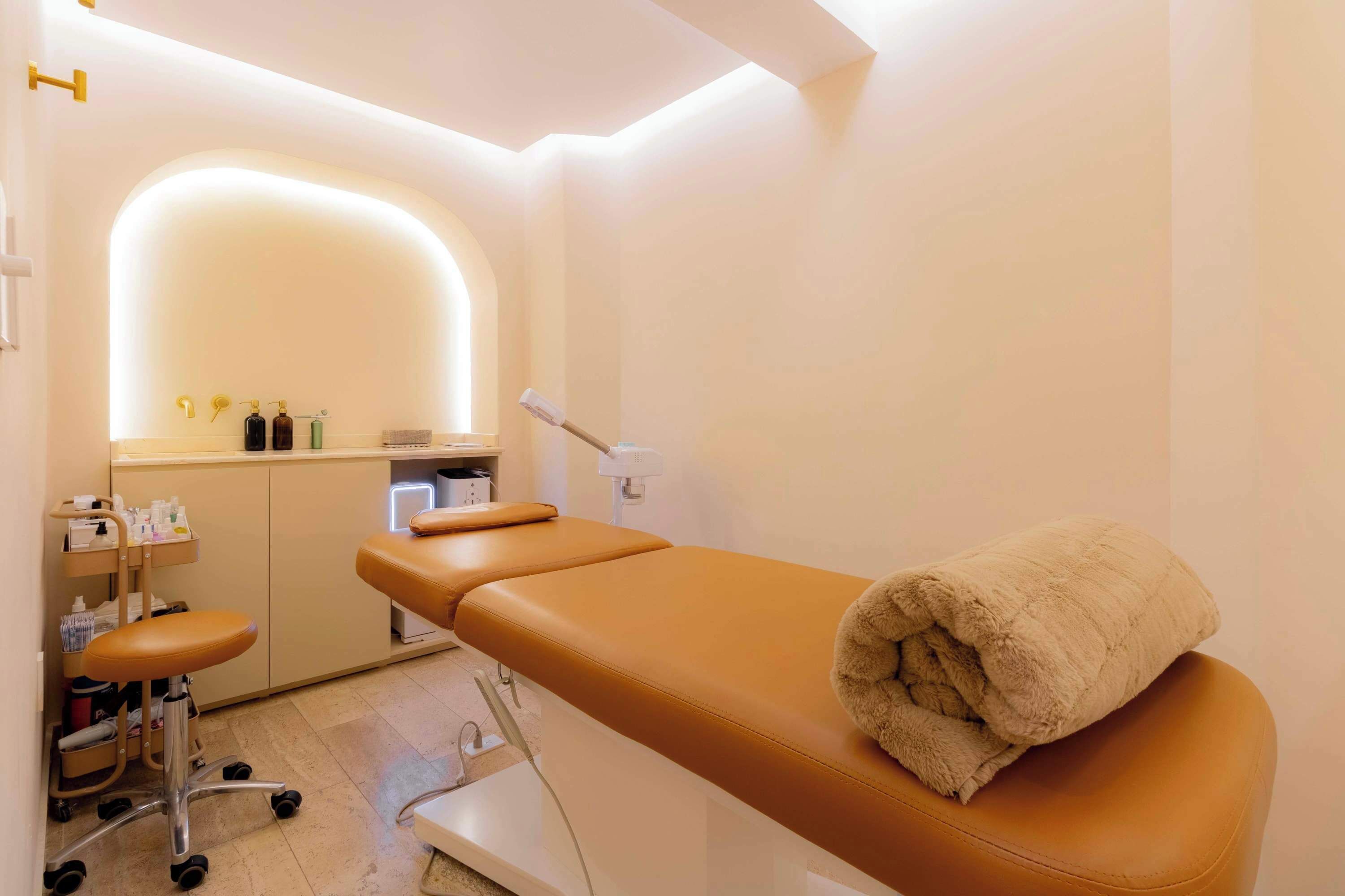 Una sala visite moderna e pulita, con un lettino da visita, un piccolo bancone con materiale medico e uno sgabello.