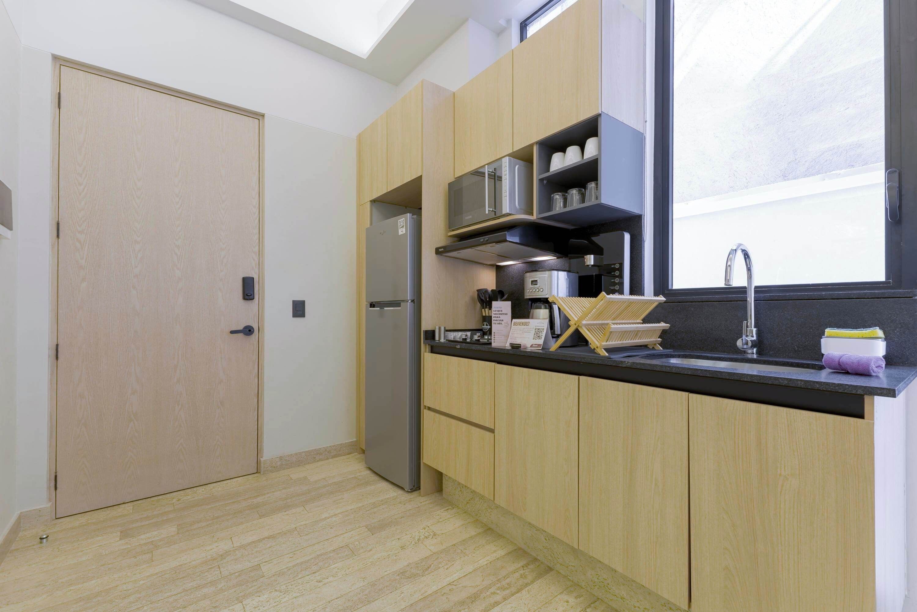 Une cuisine moderne avec des meubles en bois, un réfrigérateur en acier inoxydable, un four à micro-ondes et un évier placé sous une fenêtre.