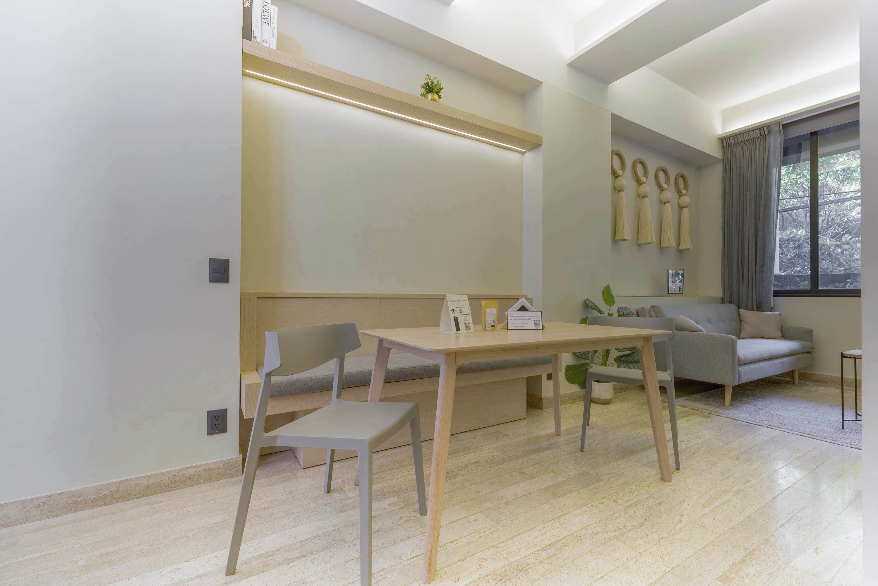 Un salon moderne avec une table en bois, deux fauteuils gris, un canapé gris et une fenêtre avec des rideaux.