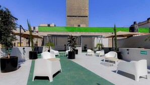 A rooftop terrace with white plastic chairs and tables, potted plants, and a view of a tall building in the background. - Capitalia | Chill Stay & Near Condesa & Museums (Ciudad de México)